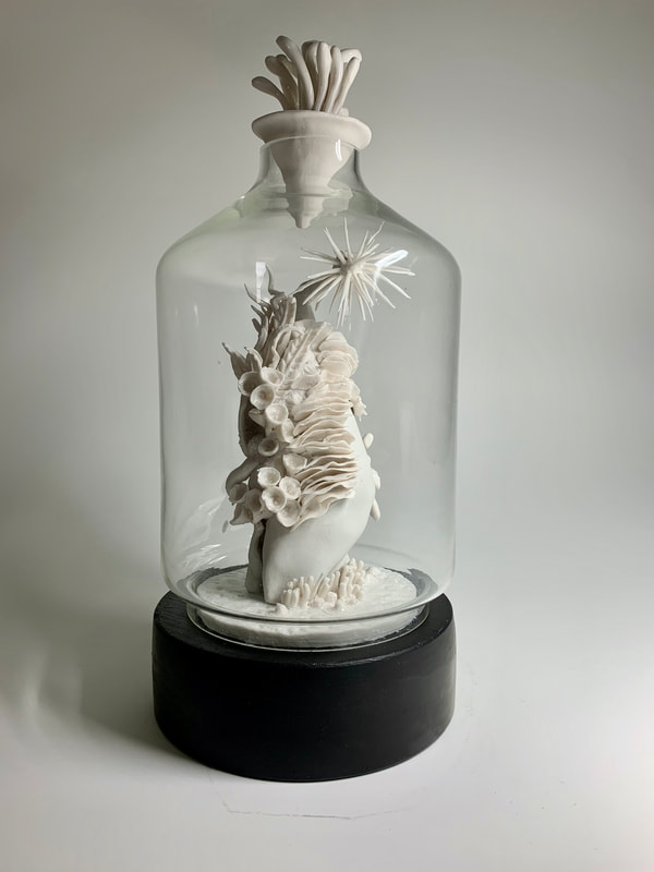 a bell jar that holds a small ceramic sculpture made of natural shaped objects overtaking a body shape